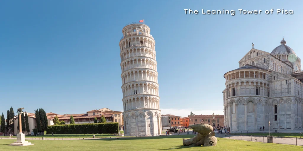 The world-famous Leaning Tower of Pisa and the adjacent cathedral standing on a green lawn against a sunset sky.