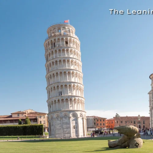 The world-famous Leaning Tower of Pisa and the adjacent cathedral standing on a green lawn against a sunset sky.