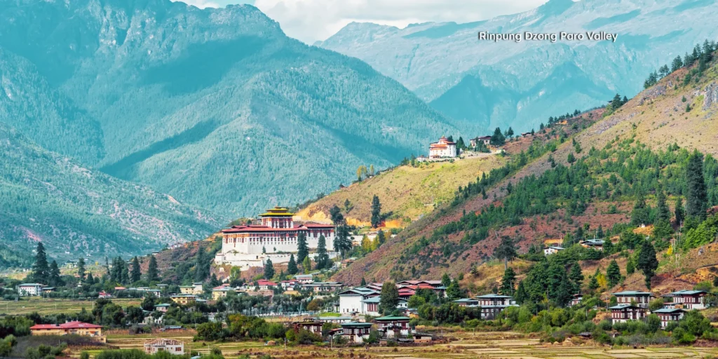 Scenic view of Rinpung Dzong fortress and a traditional wooden cantilever bridge in Paro Valley.