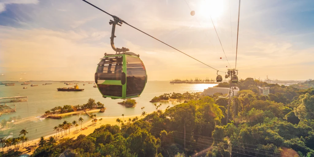 An aerial cable car crossing the water towards Sentosa Island during a beautiful golden sunset.