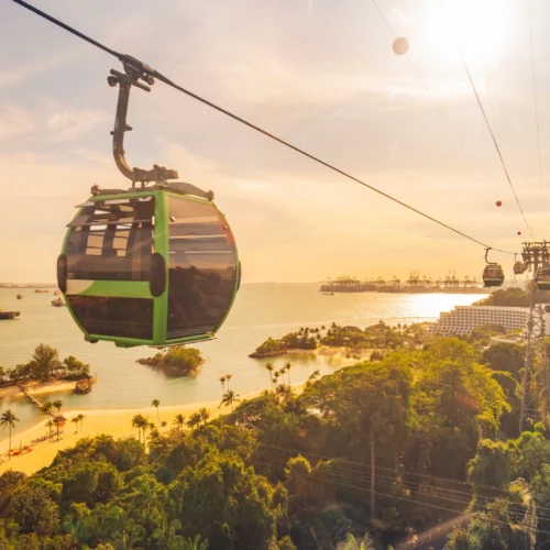 An aerial cable car crossing the water towards Sentosa Island during a beautiful golden sunset.