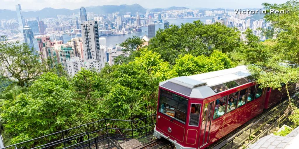 The historic red Peak Tram ascending Victoria Peak with a stunning view of Hong Kong's skyscrapers in the background.