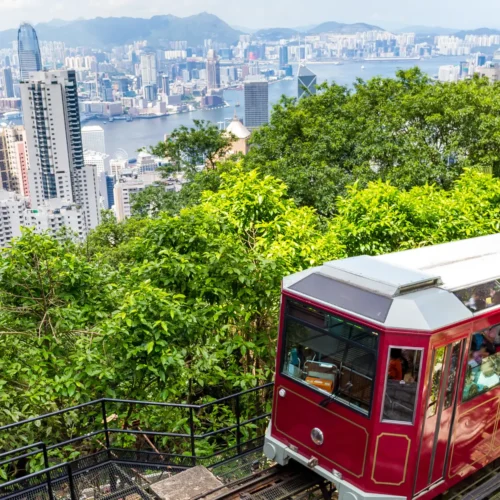The historic red Peak Tram ascending Victoria Peak with a stunning view of Hong Kong's skyscrapers in the background.
