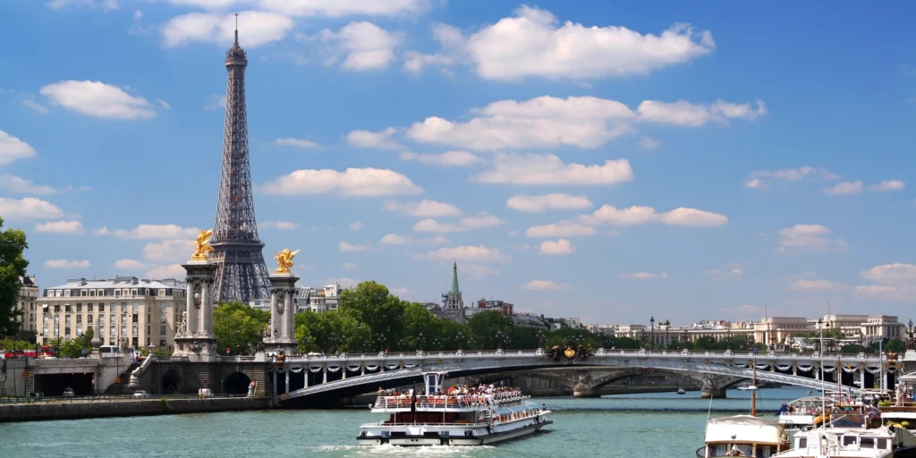 Illuminated Eiffel Tower at night with sightseeing cruise boat on the Seine River during Paris tour from Chennai.