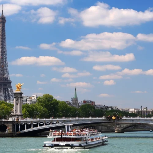 Illuminated Eiffel Tower at night with sightseeing cruise boat on the Seine River during Paris tour from Chennai.