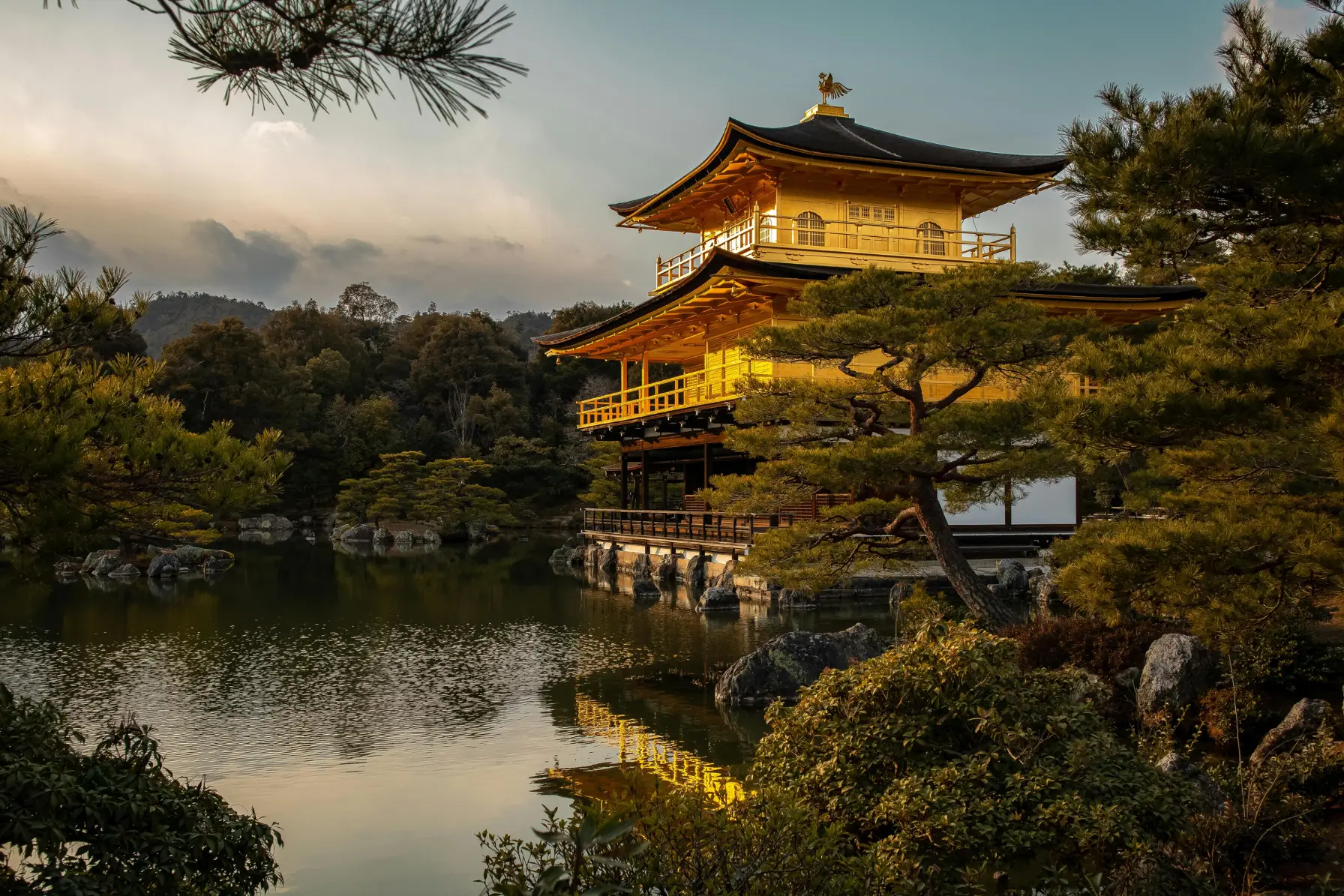 Gold-leaf covered Kinkaku-ji Golden Pavilion reflecting in the Mirror Pond surrounded by pine trees in Kyoto