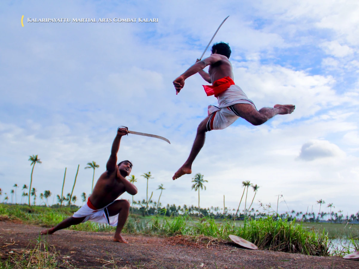 Martial artists performing acrobatic sword and shield combat inside a traditional Kalari arena Kerala